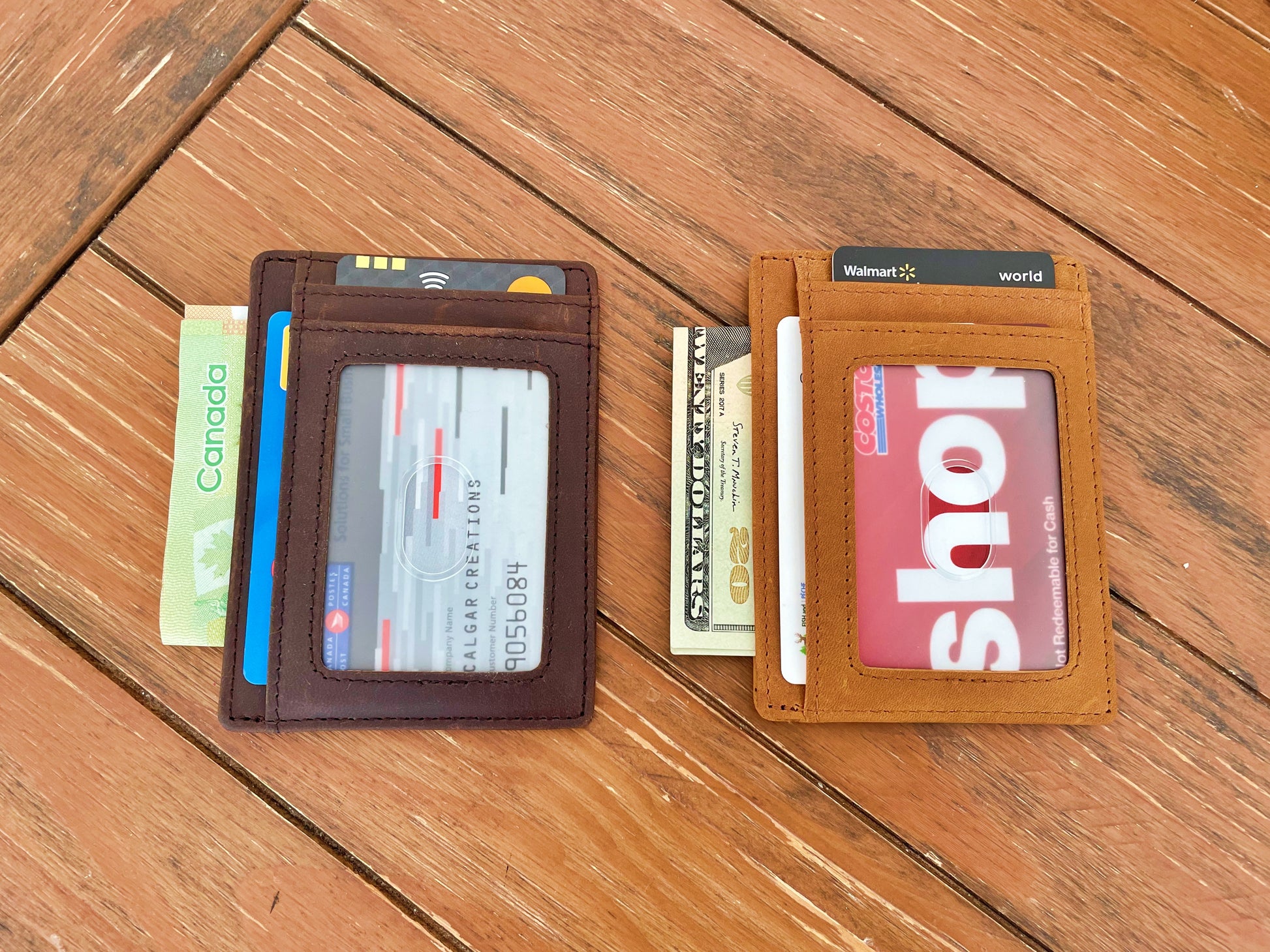 Two slim leather card wallets displayed side-by-side on a wooden surface. The left wallet is dark brown and holds credit cards and cash.
