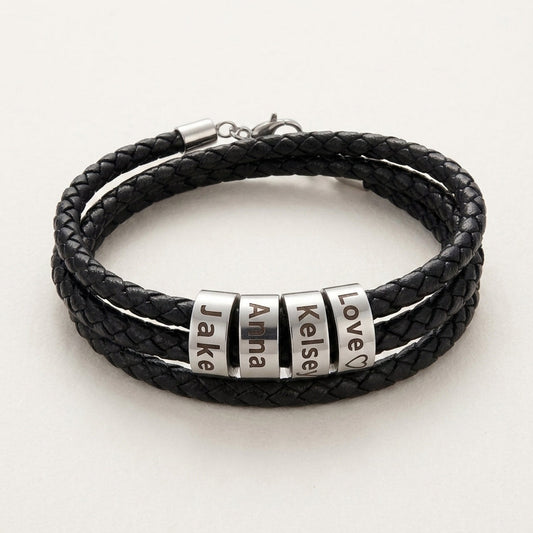 A multi-strand black braided leather bracelet with four silver metal nameplates engraved with the names 'Jake', 'Anna', 'Kelsey', and 'Love', displayed on a light off-white background.
